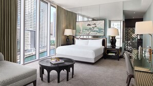 A hotel room with a large bed, a round coffee table, a desk with a lamp, and a view of the city through large windows. - W Miami (Miami)