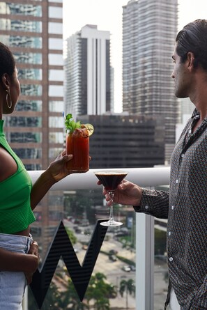 Two people holding drinks on a balcony with a city view.