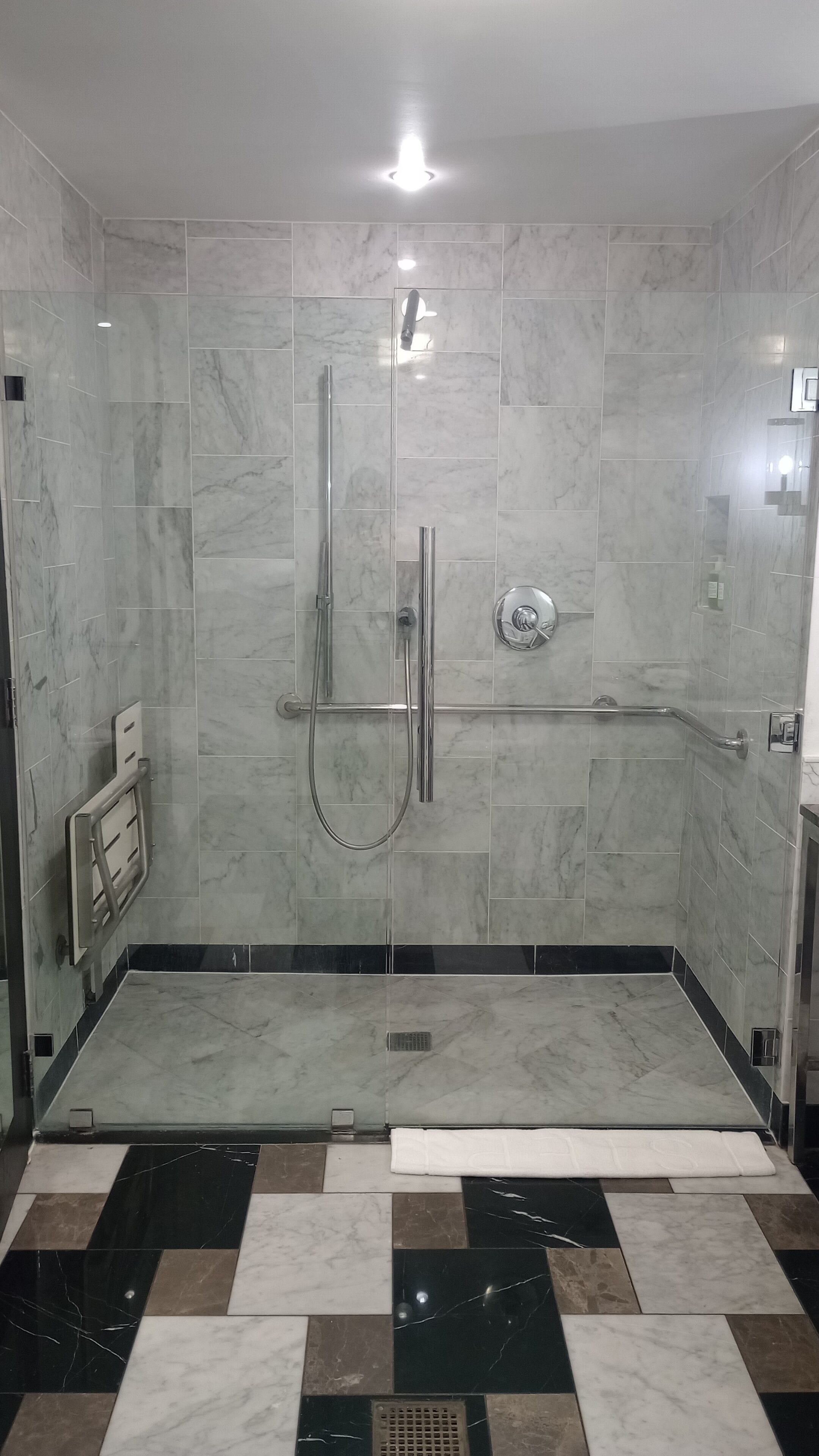 A modern bathroom with a shower, a handrail, and a tiled floor.