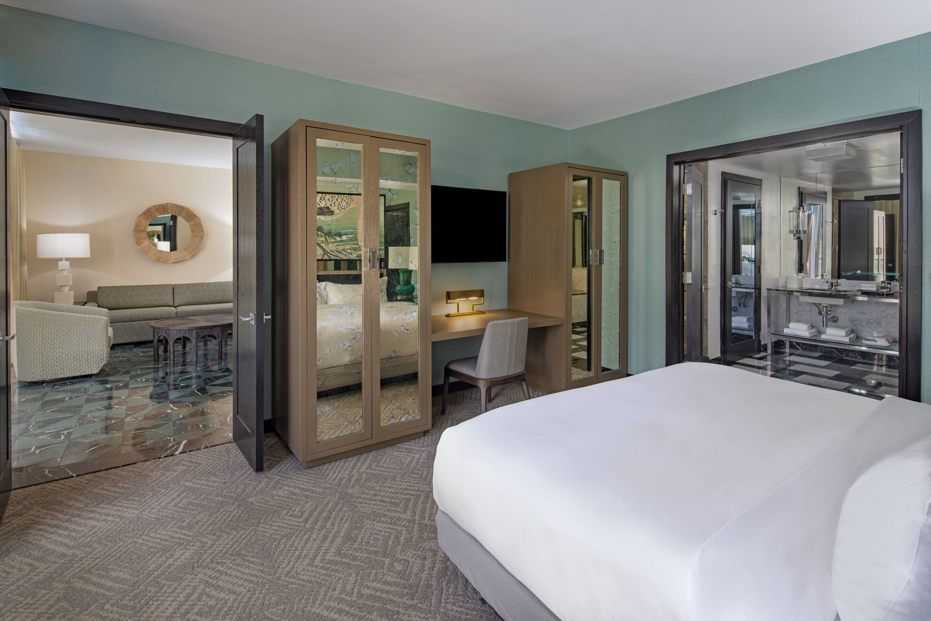 A hotel room with a large bed, a desk with a chair, a TV, and a wardrobe.