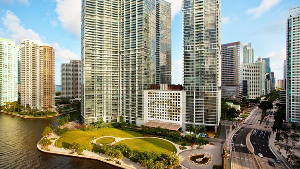 A high-rise building with a modern glass facade, surrounded by a landscaped area with a water body and a curved road. - W Miami (Miami)