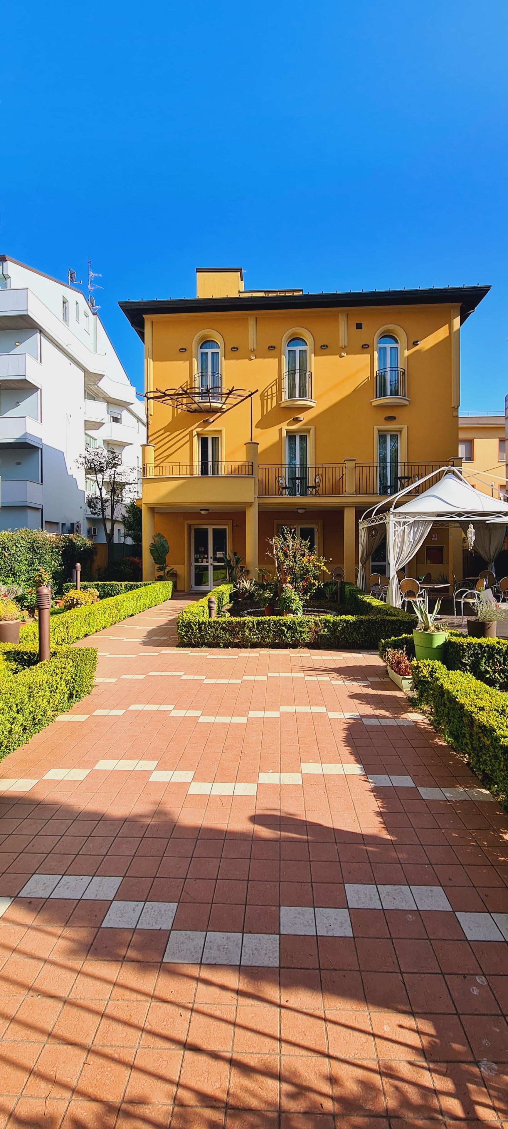 A yellow building with a paved walkway leading to a covered outdoor seating area.