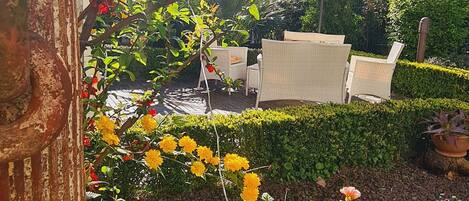 Un jardin agrémenté de diverses plantes à fleurs, d’un grand pot décoratif et d’un espace détente avec des chaises.