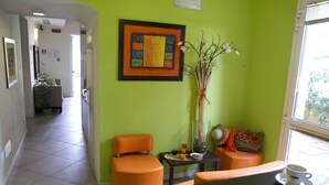 A reception area with a green wall, a framed artwork, a vase with branches, and a seating area with a table and a cup. - Hotel Alibì (Rimini)