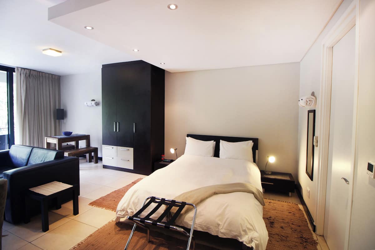 Quarto de hotel moderno com uma cama grande, escrivaninha, cadeira, guarda-roupa e banheiro.