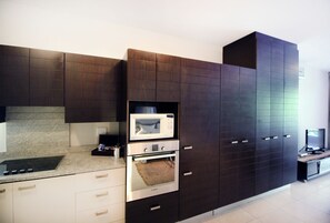 A modern kitchen with dark cabinetry, a built-in microwave, oven, and a small television on a wooden stand.