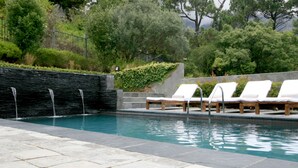 A swimming pool with a waterfall feature, surrounded by a stone wall and lush greenery. - The Glen Apartments (Cape Town)