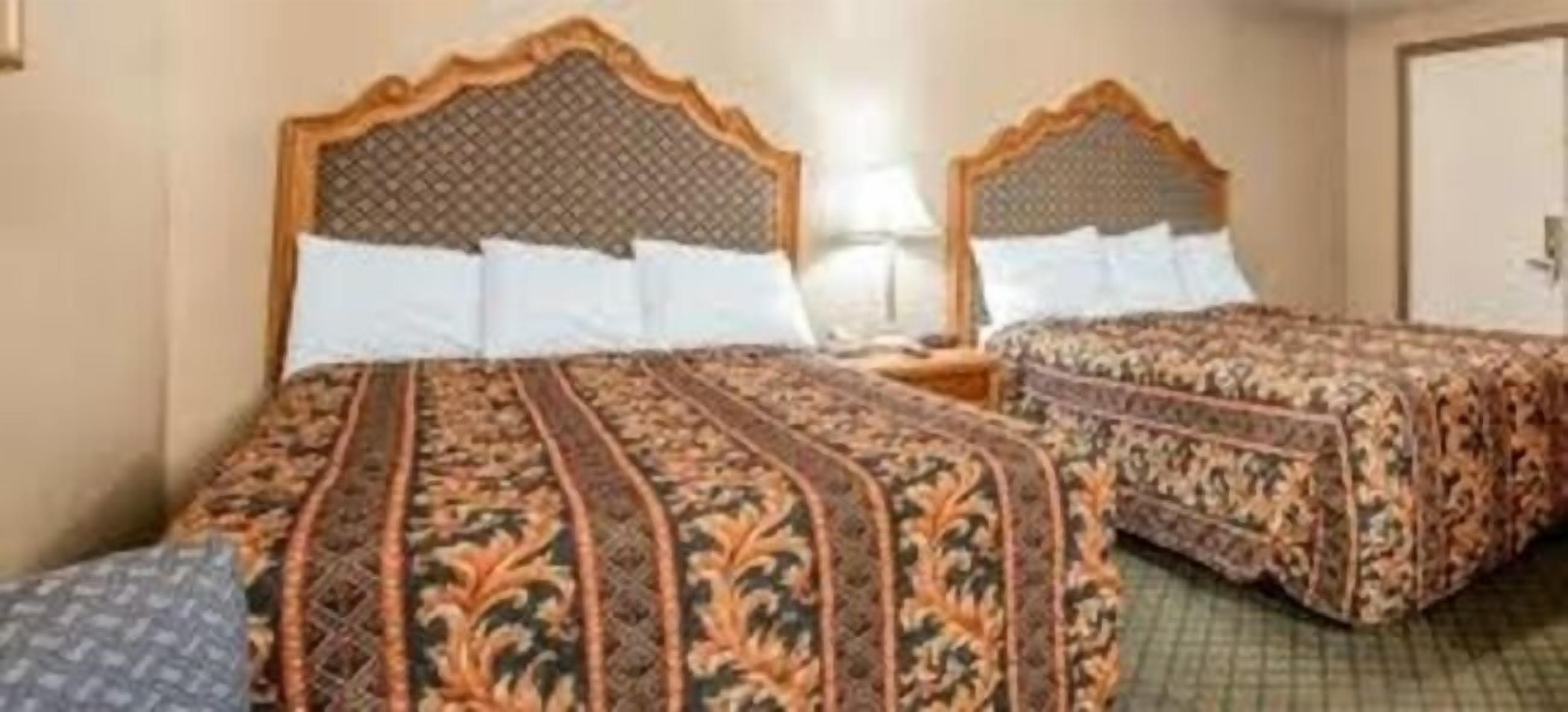 A hotel room with two beds, each with a patterned bedspread and a wooden headboard.