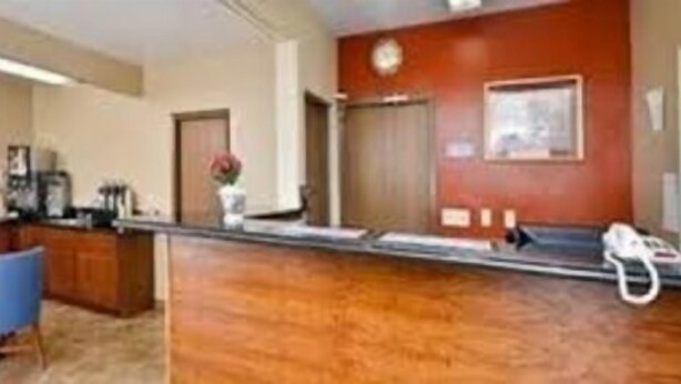 A reception area with a wooden reception desk, blue chairs, a clock, and a door. - Riverton Inn & Suites (Riverton)