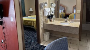 A hotel room with a bed, a bathroom with a sink and mirror, and a door leading to another room. - Riverton Inn & Suites (Riverton)