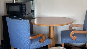 A small room with a round wooden table, two blue upholstered chairs, a microwave, and a large mirror on the wall. - Riverton Inn & Suites (Riverton)