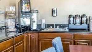 A kitchen with wooden cabinets, a refrigerator, a coffee machine, and a coffee dispenser. - Riverton Inn & Suites (Riverton)