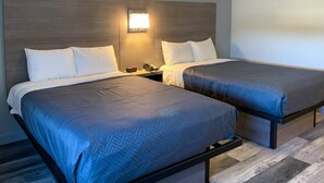 A hotel room with two beds, each with a headboard and a bedside table. There is a wall-mounted light above the beds. - Suburban Studios near Panama City Beach (Panama City)