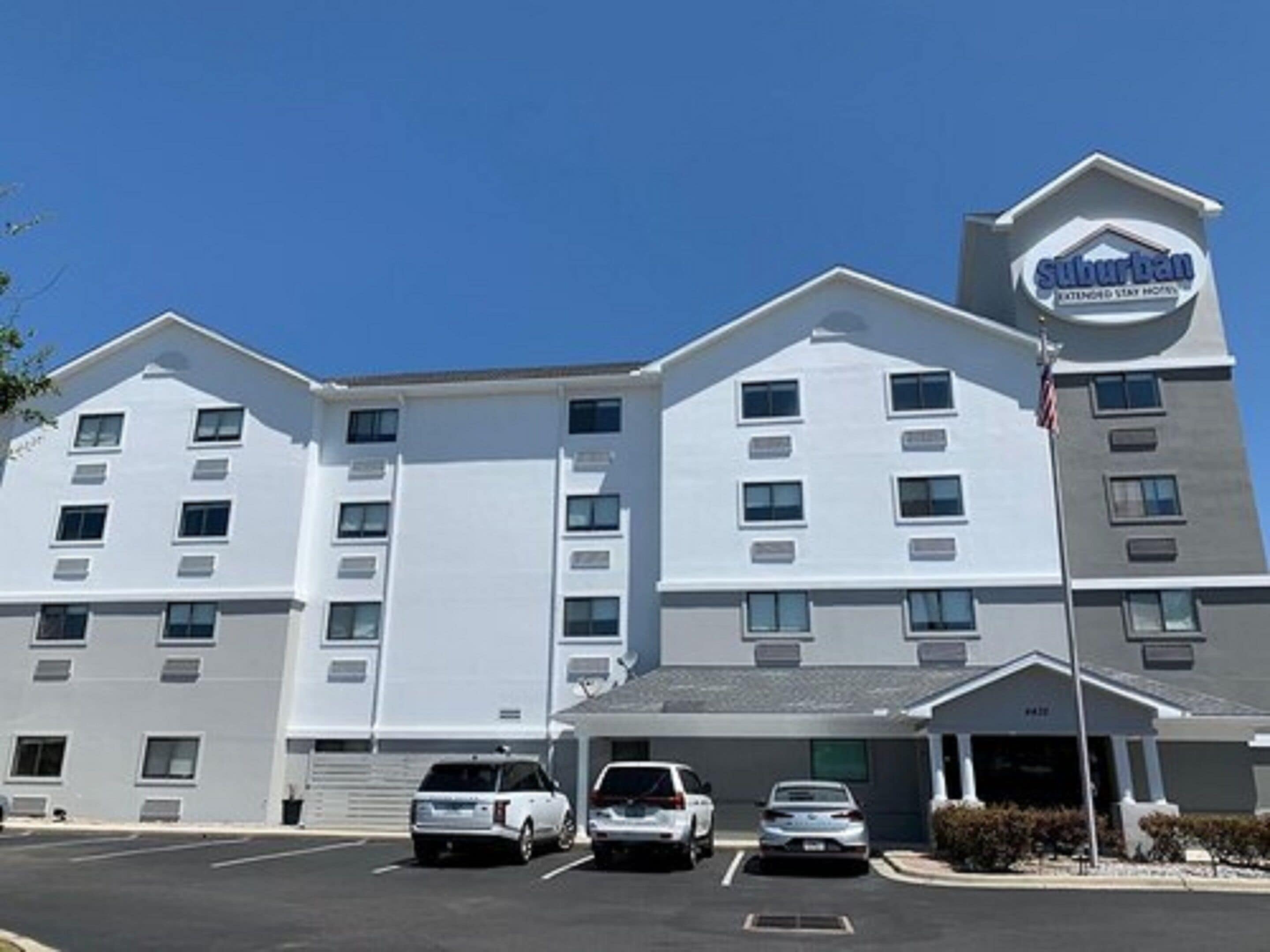 A suburban extended stay hotel with a modern design, featuring multiple parking spaces and a clear sky.