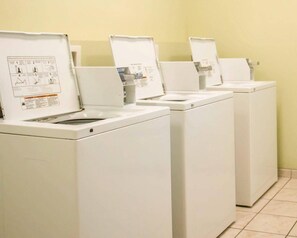 A row of white front-loading washing machines in a room with yellow walls and tiled flooring.