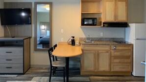 A compact kitchen with a microwave, sink, and refrigerator. There's a dining table with chairs and a TV mounted on the wall. - Suburban Studios near Panama City Beach (Panama City)