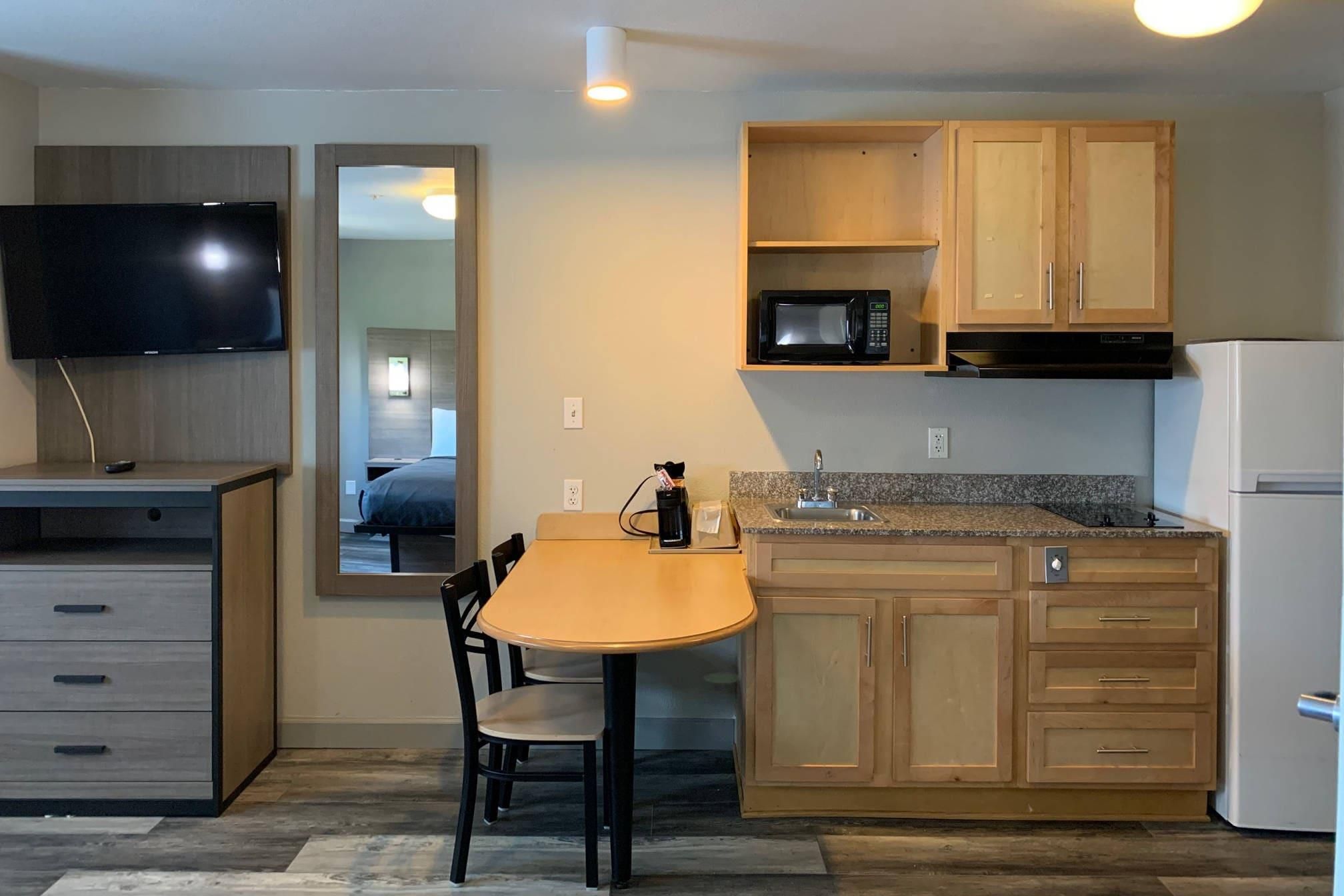 Cocina funcional con microondas, pileta y heladera. Hay una mesa de comedor con sillas y un televisor montado sobre ella.