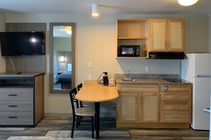 A compact kitchen with a microwave, sink, and refrigerator. There's a dining table with chairs and a TV mounted above it. - Suburban Studios near Panama City Beach (Panama City)