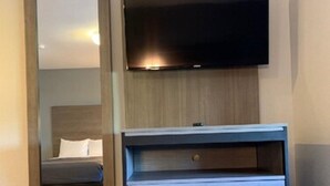 A modern hotel room with a large mirror, a flat-screen TV mounted on the wall, and a light-colored dresser with three drawers. - Suburban Studios near Panama City Beach (Panama City)