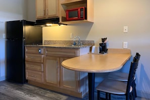 Cocina compacta con refrigerador negro, microondas, fregadero y una pequeña mesa de comedor con sillas.