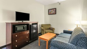 Ein kompaktes Hotelzimmer mit Fernseher auf einer Kommode, einer Mikrowelle, einem kleinen Tisch, einer Couch und einem gestreiften Sessel.