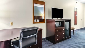 Ein Hotelzimmer mit Schreibtisch, Stuhl, Fernseher, Minibar und Spiegel.
