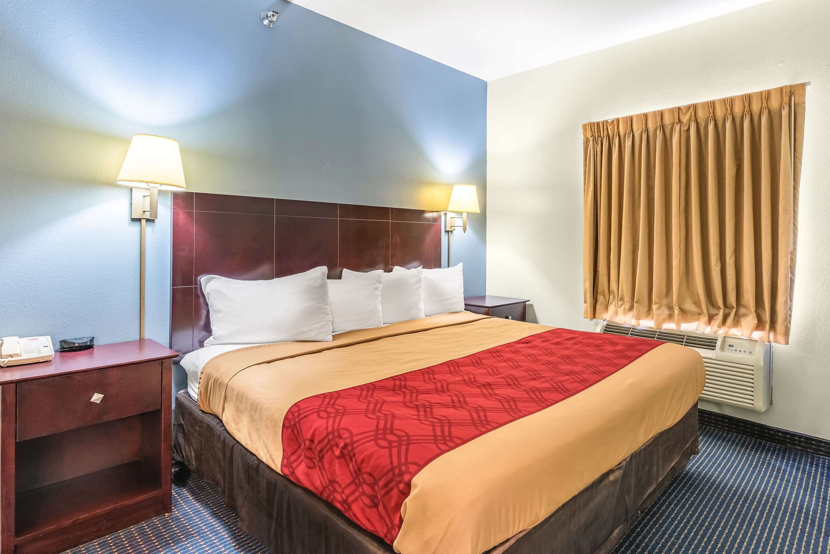 Habitación de hotel con una cama grande, dos mesitas de noche, una lámpara de pared, una ventana con cortinas y un equipo de aire acondicionado.