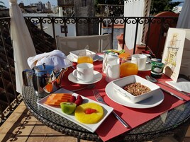 Ein Esstisch mit verschiedenen Früchten, Getränken und Frühstücksartikeln auf einem Balkon.