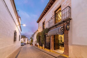 Una calle estrecha flanqueada por edificios, con un restaurante que destaca por su toldo a rayas y una señal visible.