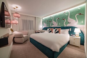 A modern hotel room with a large bed, a sitting area, a vanity, and a wall mural of swans.
