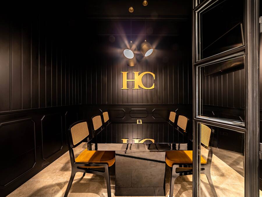 A conference room with a glass table, wooden chairs, and a black wall with the letters "HC" illuminated.