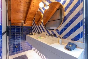 Een badkamer met een houten plafond, een grote spiegel en een wand betegeld in blauw en wit.
