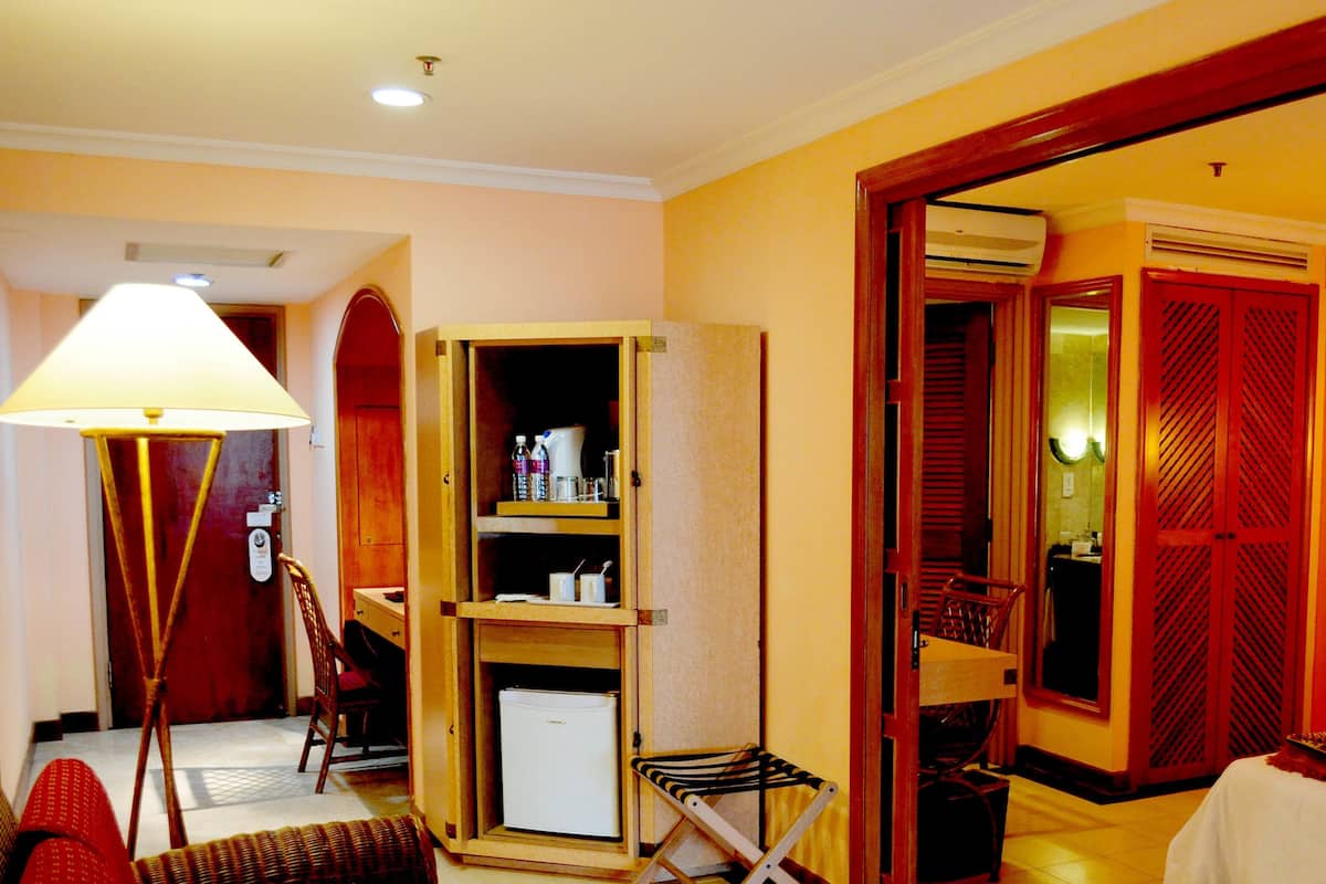 A hotel room with a bed, a desk, a chair, a small refrigerator, a lamp, and a wardrobe.