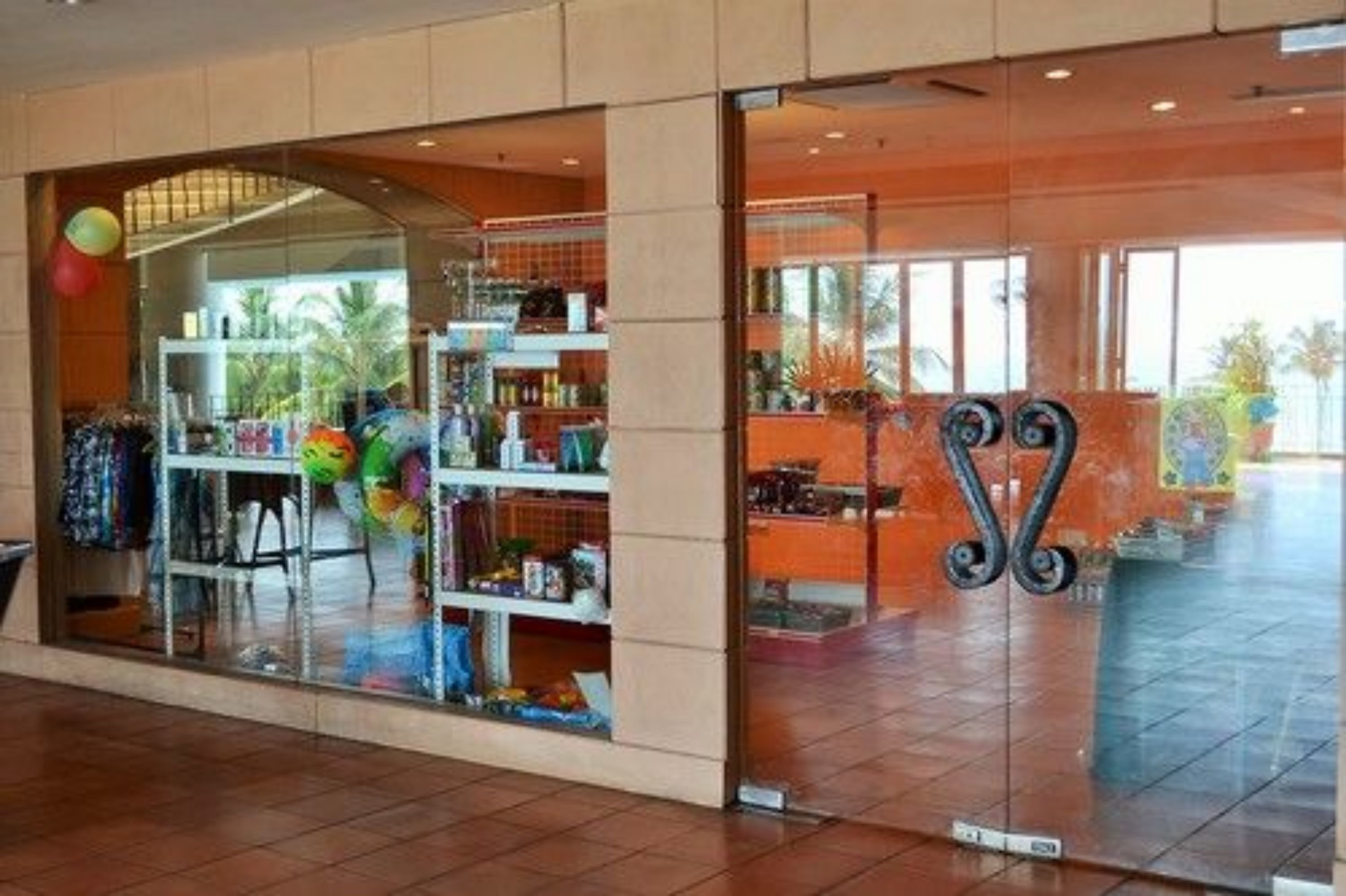 A hotel lobby with a glass storefront displaying colorful items, a tiled floor, and a large decorative metal structure.