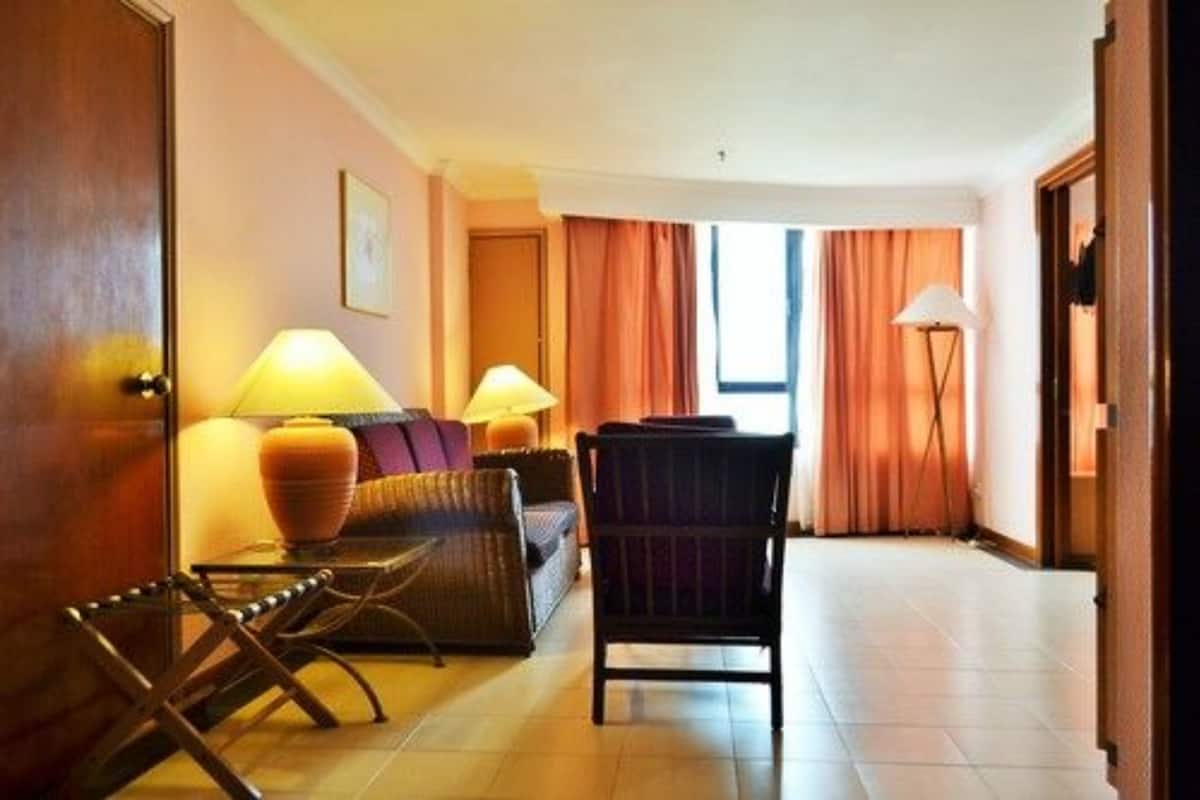 A hotel room with a sofa, armchairs, a lamp, and a window with curtains.