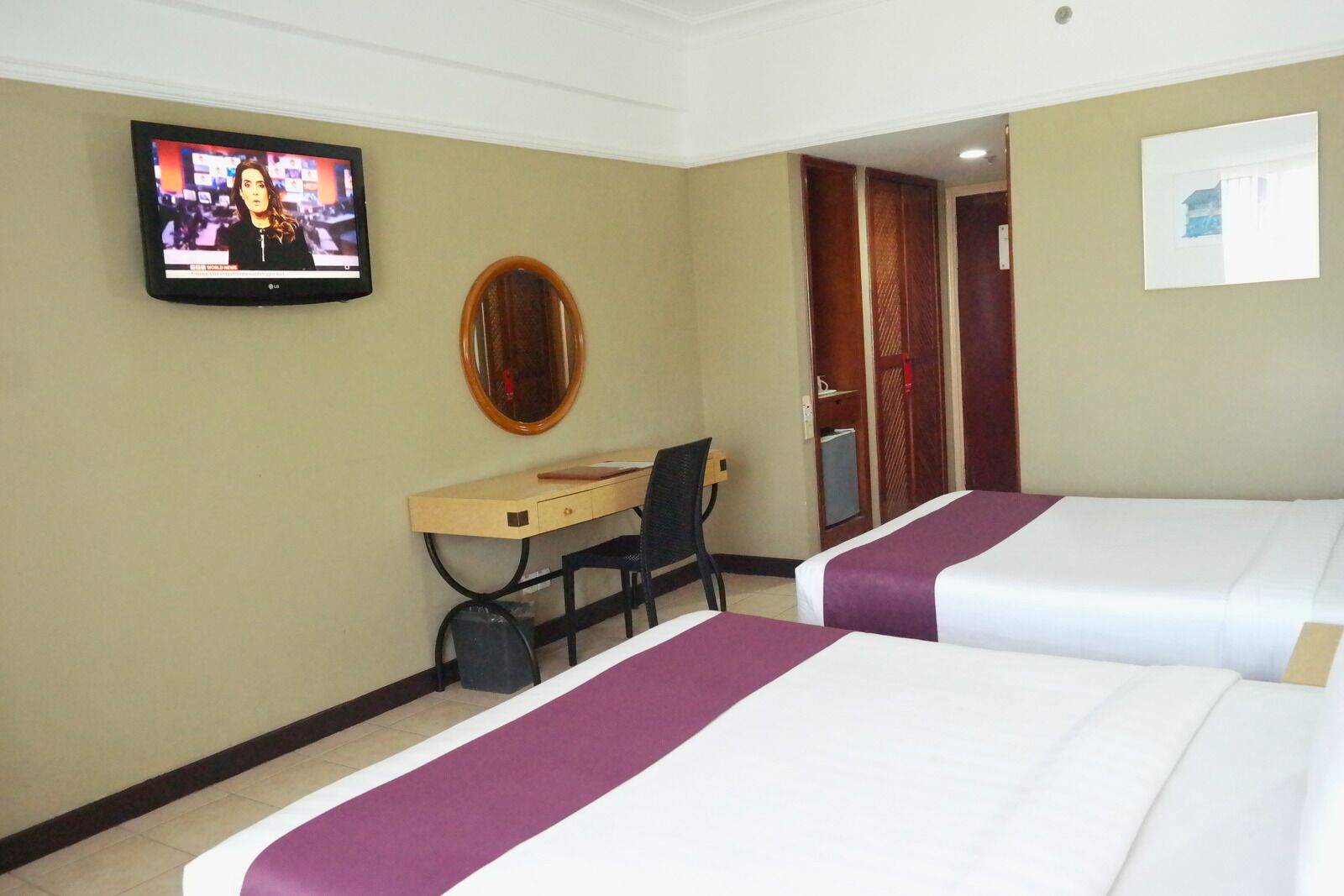 Een hotelkamer met twee bedden, een bureau, een stoel, een televisie en een spiegel.