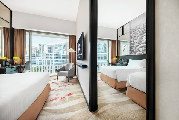 A hotel room with a large window, a desk with a lamp, a bed, and a chair.