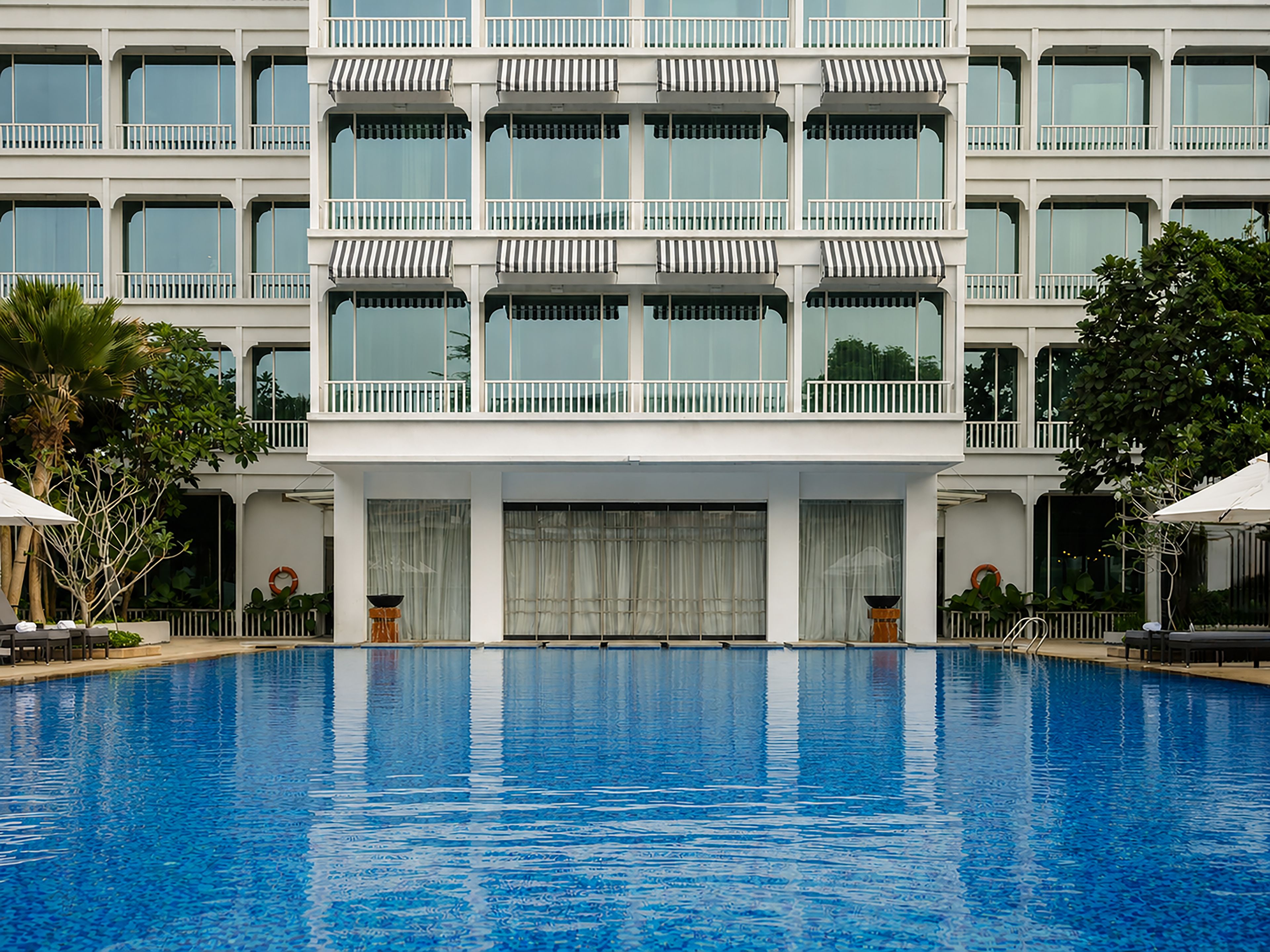 A hotel with a large swimming pool, multiple balconies with striped awnings, and a white facade.
