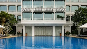 A hotel with a large swimming pool, multiple balconies with striped awnings, and a white facade.