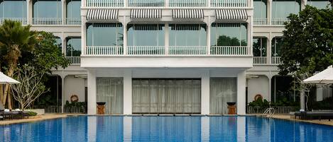 A hotel with a large swimming pool, multiple balconies with striped awnings, and a white facade.