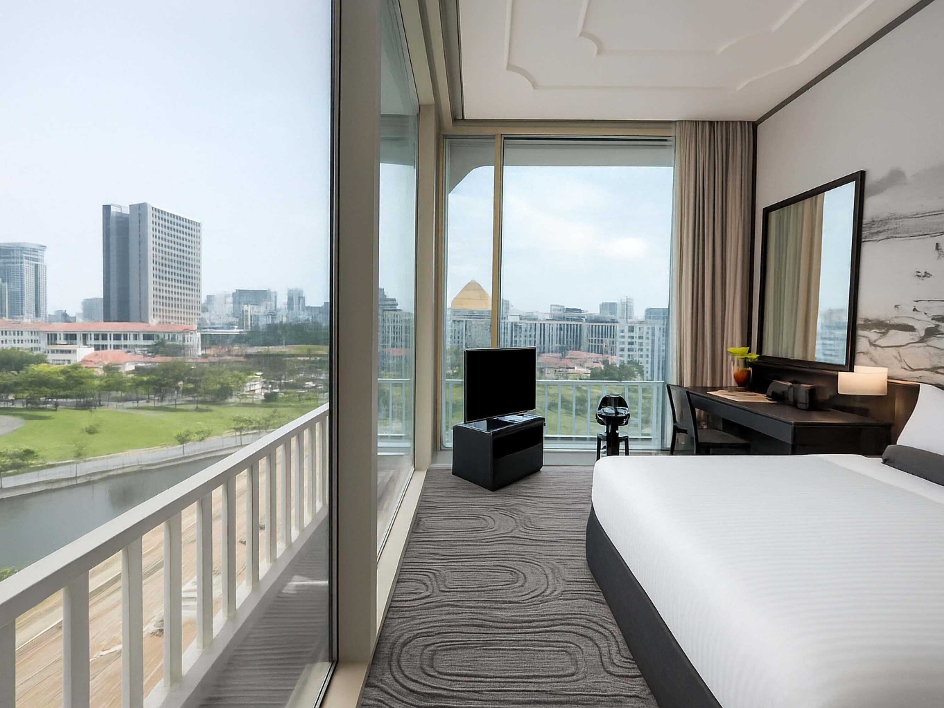 A hotel room with a large bed, a desk with a computer, a TV, and a view of a cityscape.
