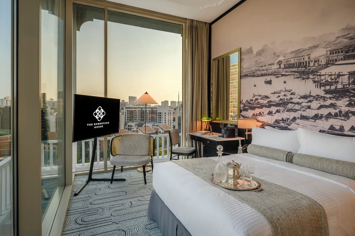 Habitación de hotel con una cama grande, un escritorio, una silla, un televisor y vistas a la ciudad.
