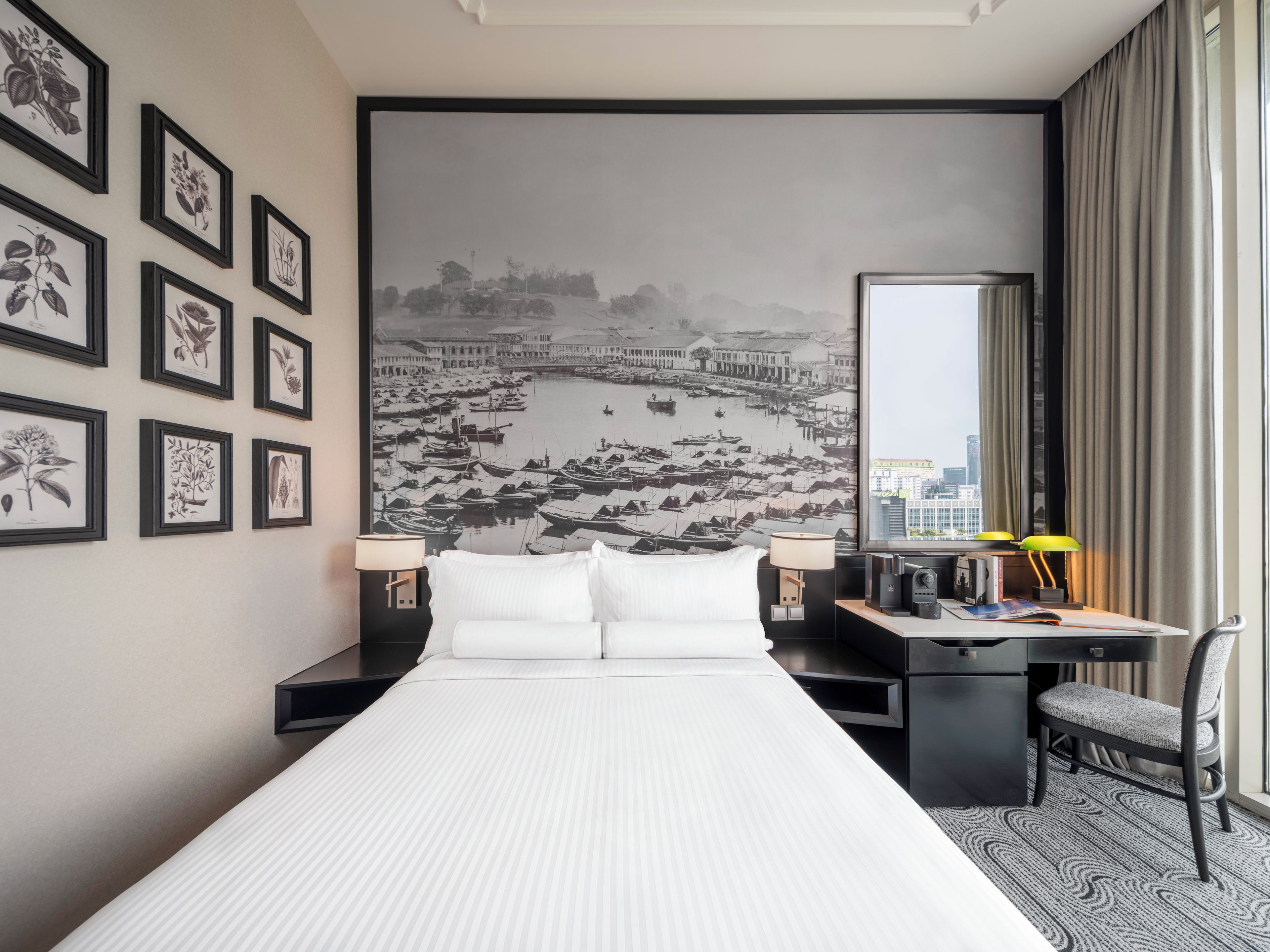 A hotel room with a bed, desk, chair, and artwork on the walls.