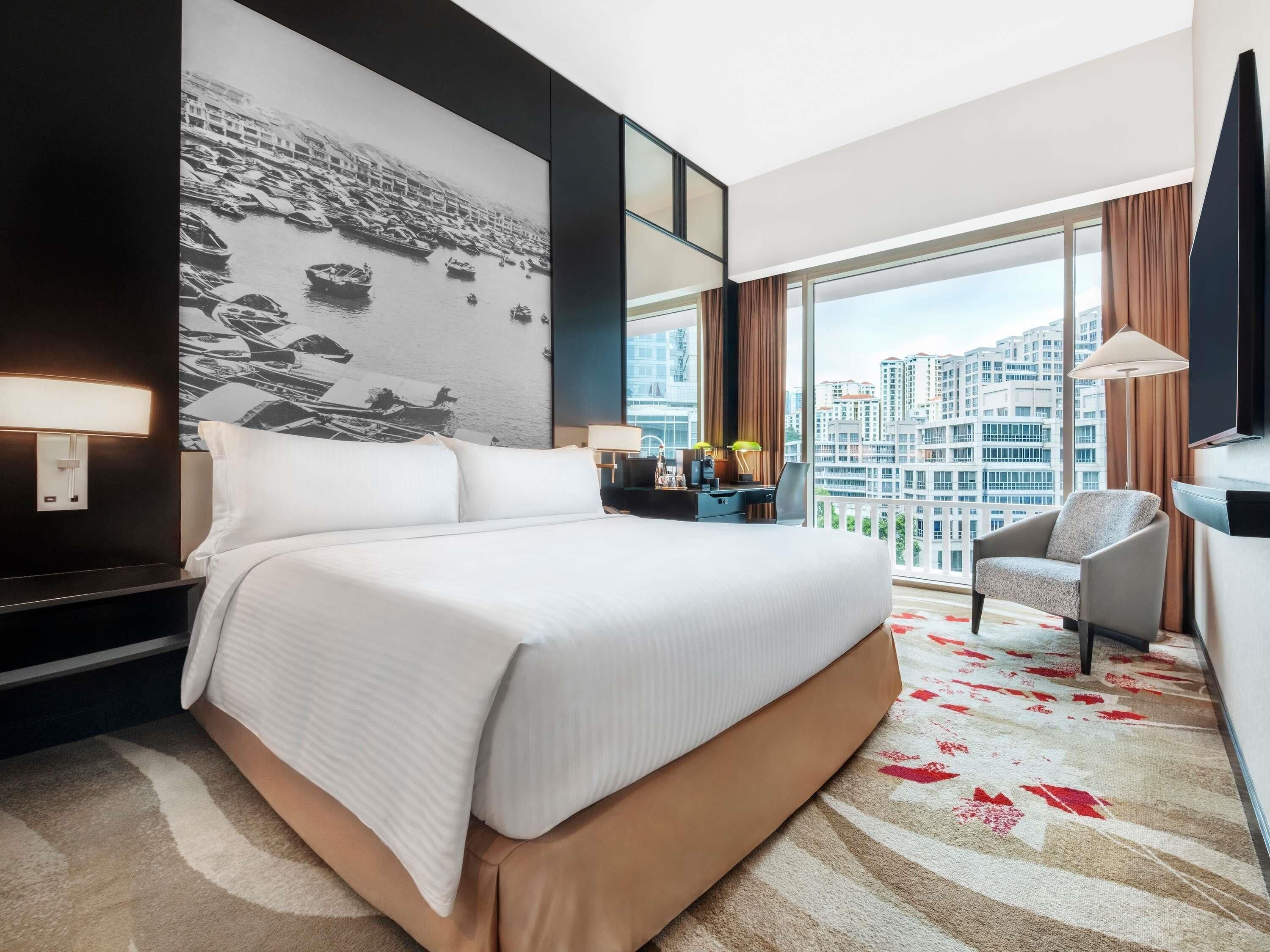 A hotel room with a large bed, a desk, a chair, and a view of the city.