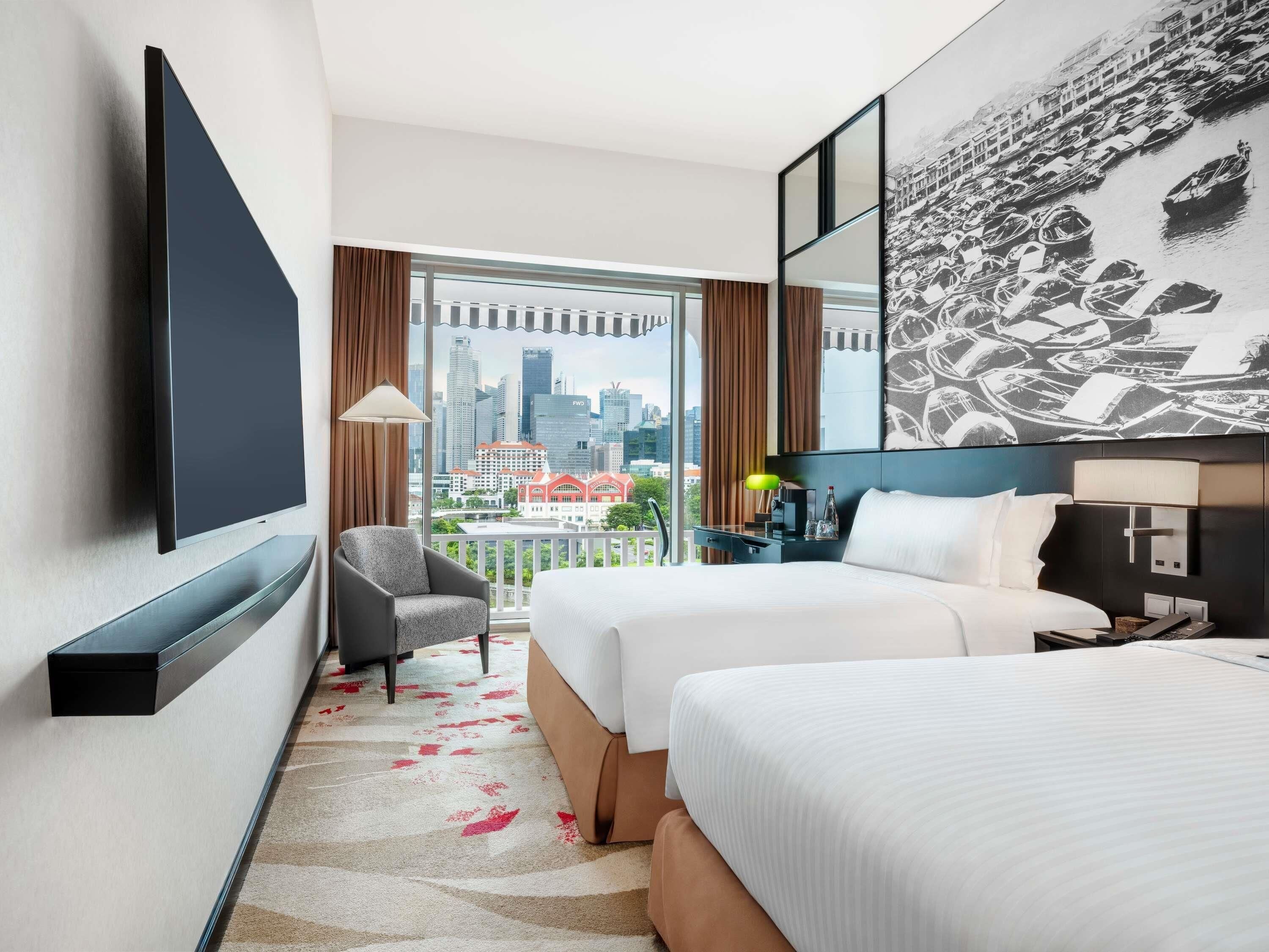 A hotel room with a city view, two beds, a desk, and a TV.