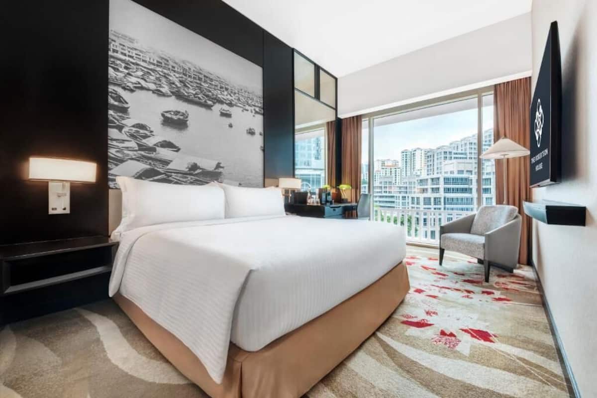 Habitación de hotel con una cama grande, un televisor de pantalla plana, un escritorio con lámpara, una silla y vistas a la ciudad.