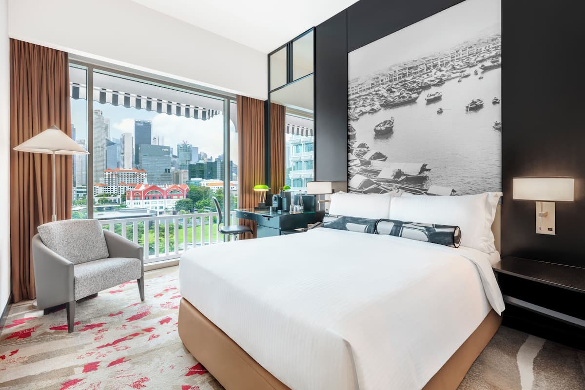 A hotel room with a large bed, a chair, a desk, and a view of the cityscape.