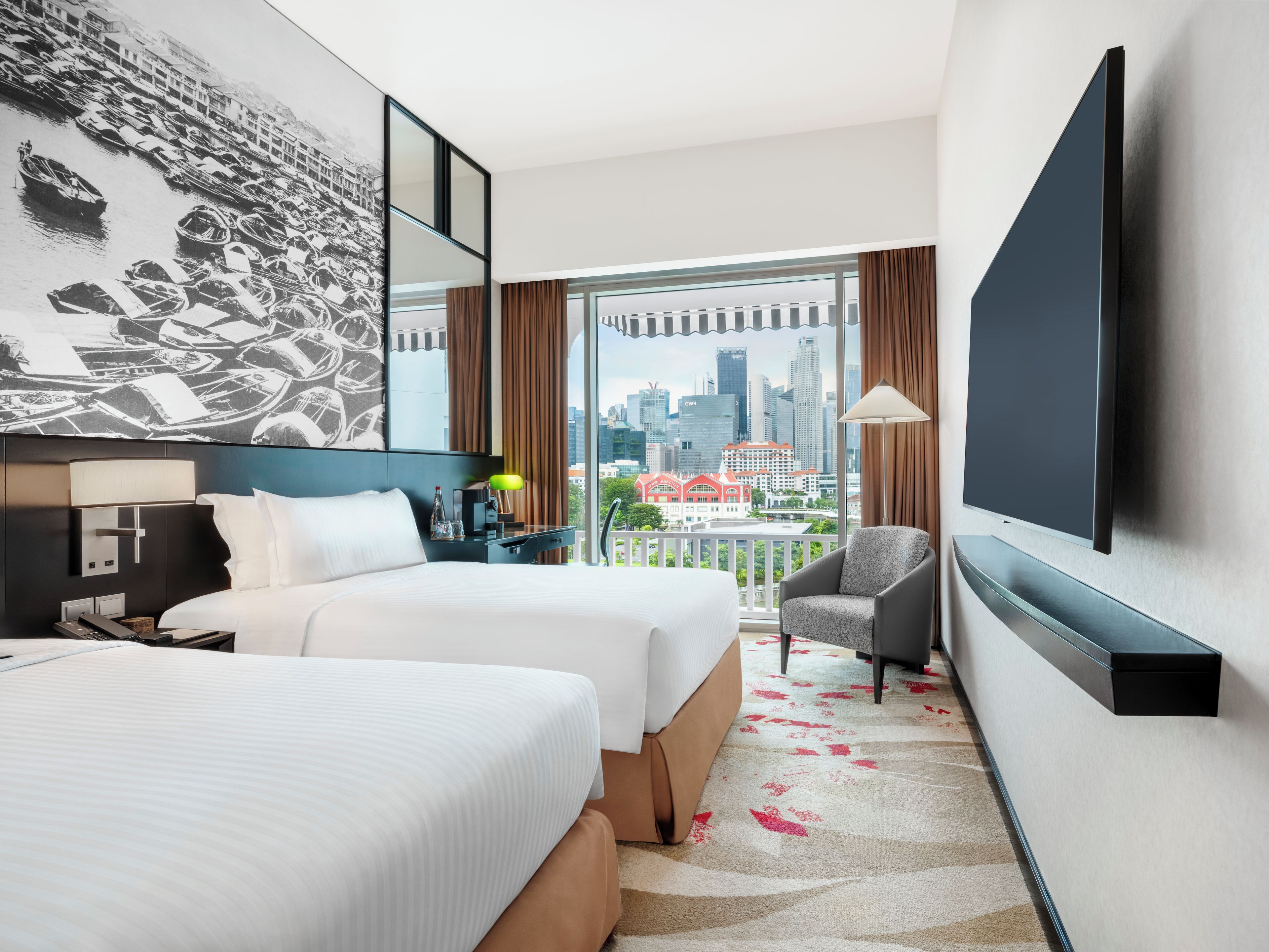 A hotel room with two beds, a large window with a city view, a flat-screen TV, and a balcony with a view of the city skyline.