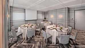 A conference room with round tables, chairs, a projector screen, and a patterned carpet. - Novotel Singapore Robertson Quay (Singapore)