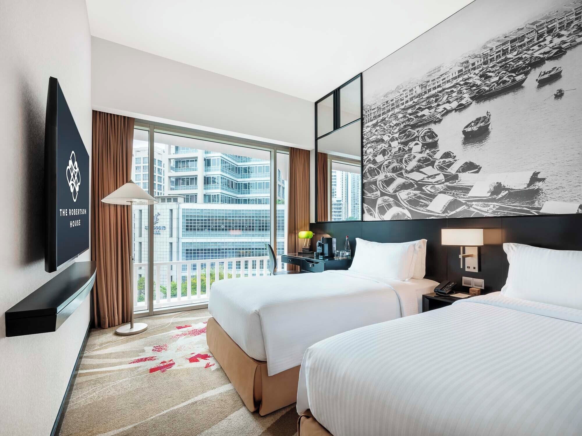 Habitación de hotel con dos camas, televisión, escritorio, lámpara y una ventana grande con vistas a la ciudad.